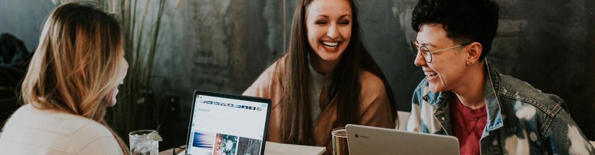 Three People Sat around a Table Laughing with a Laptop